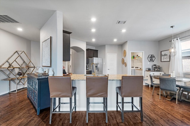 kitchen with sink, a breakfast bar area, dark hardwood / wood-style floors, light stone countertops, and stainless steel fridge with ice dispenser