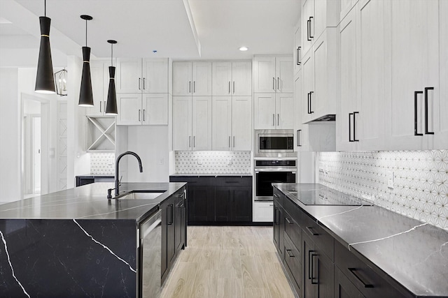 kitchen with stainless steel appliances, sink, white cabinets, hanging light fixtures, and an island with sink