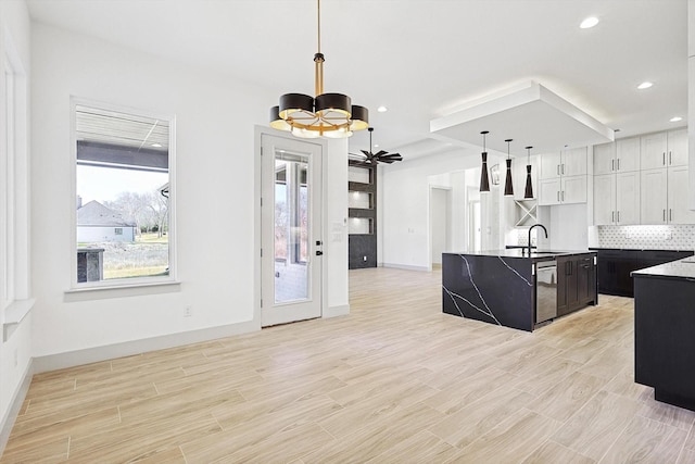 kitchen featuring a kitchen island with sink, sink, pendant lighting, a notable chandelier, and white cabinetry