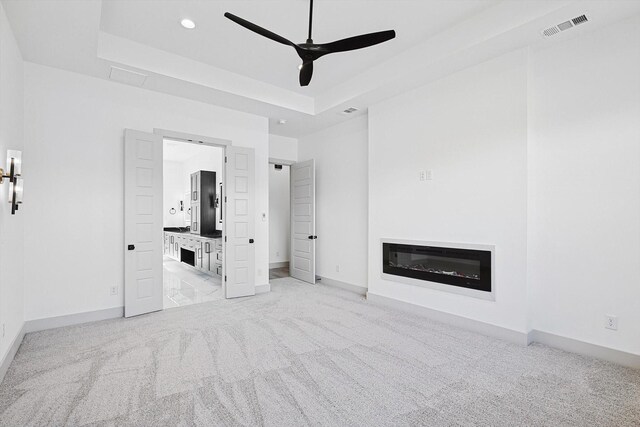 unfurnished living room featuring a raised ceiling, ceiling fan, and light carpet