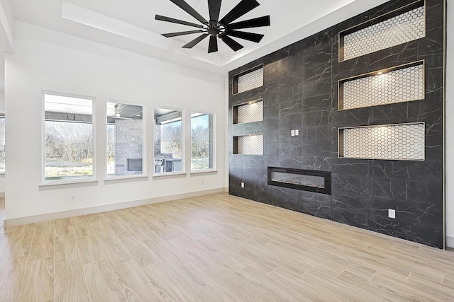 spare room featuring ceiling fan, a raised ceiling, a high end fireplace, and light hardwood / wood-style flooring