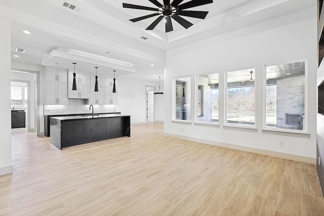 kitchen with ceiling fan, a kitchen island with sink, sink, pendant lighting, and white cabinetry