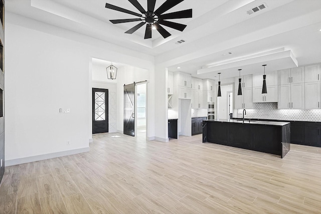 kitchen with a kitchen island with sink, ceiling fan, a tray ceiling, decorative light fixtures, and white cabinetry