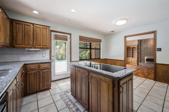 kitchen with black electric stovetop, a center island, light tile patterned flooring, and a fireplace