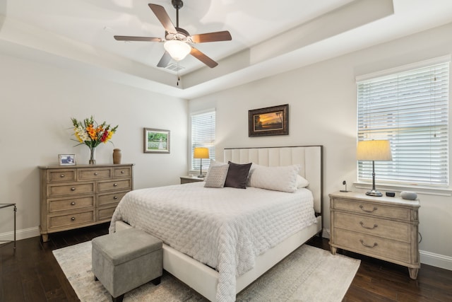 bedroom with a tray ceiling, dark wood-type flooring, and ceiling fan