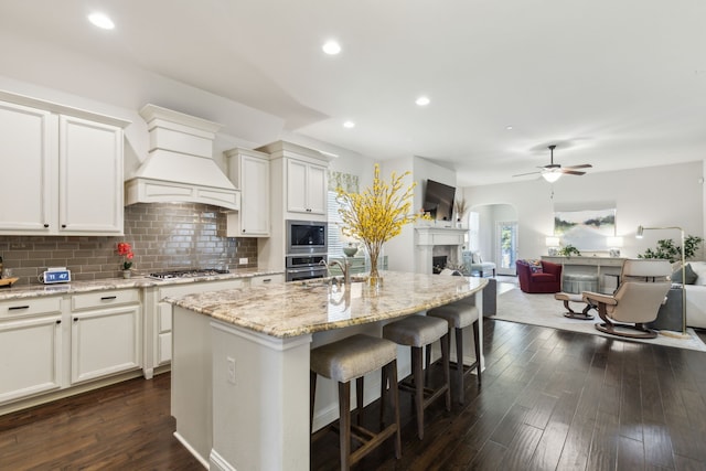 kitchen featuring white cabinetry, an island with sink, appliances with stainless steel finishes, and custom range hood