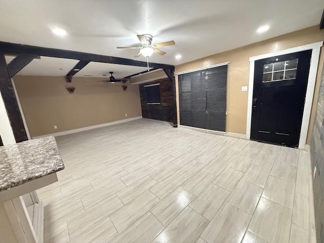 unfurnished living room featuring ceiling fan and beamed ceiling