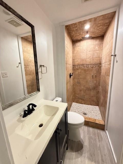 bathroom with hardwood / wood-style floors, a tile shower, vanity, and toilet