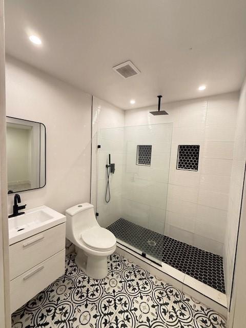 bathroom featuring tiled shower, tile patterned flooring, vanity, and toilet