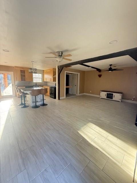 unfurnished living room featuring ceiling fan and beamed ceiling