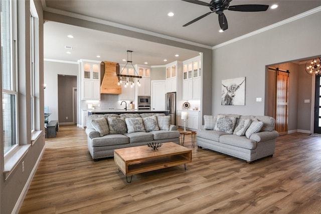 living room with ornamental molding, a barn door, sink, and ceiling fan with notable chandelier