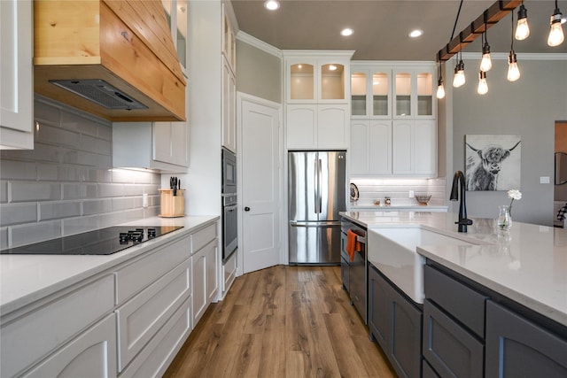 kitchen featuring appliances with stainless steel finishes, decorative light fixtures, custom range hood, and white cabinets