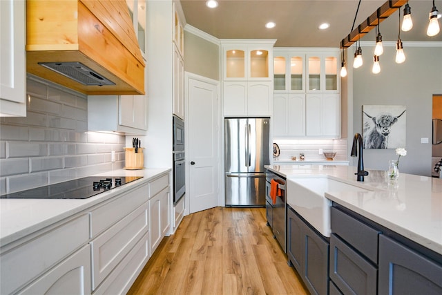 kitchen featuring white cabinetry, light countertops, appliances with stainless steel finishes, glass insert cabinets, and custom range hood