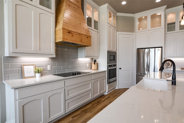 kitchen with white cabinetry, sink, backsplash, stainless steel appliances, and custom range hood