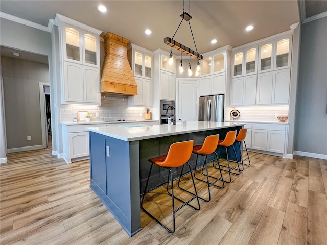 kitchen with light countertops, appliances with stainless steel finishes, a kitchen island with sink, white cabinets, and premium range hood