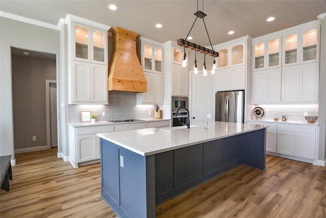 kitchen featuring premium range hood, appliances with stainless steel finishes, white cabinets, hanging light fixtures, and a center island with sink