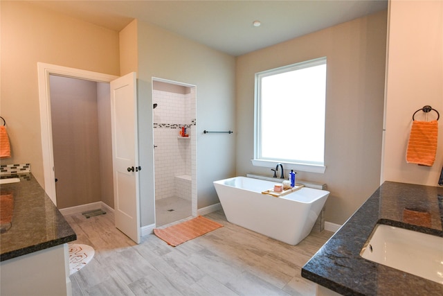 full bath featuring double vanity, a freestanding bath, a tile shower, a sink, and wood finished floors