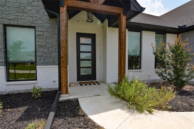 entrance to property featuring stone siding, a shingled roof, and brick siding