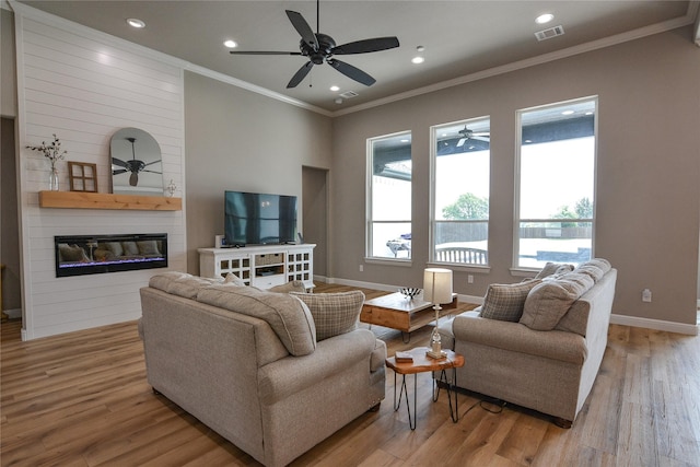 living room with crown molding, a large fireplace, ceiling fan, and light hardwood / wood-style flooring