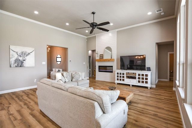 living room featuring hardwood / wood-style flooring, ceiling fan, ornamental molding, and a large fireplace