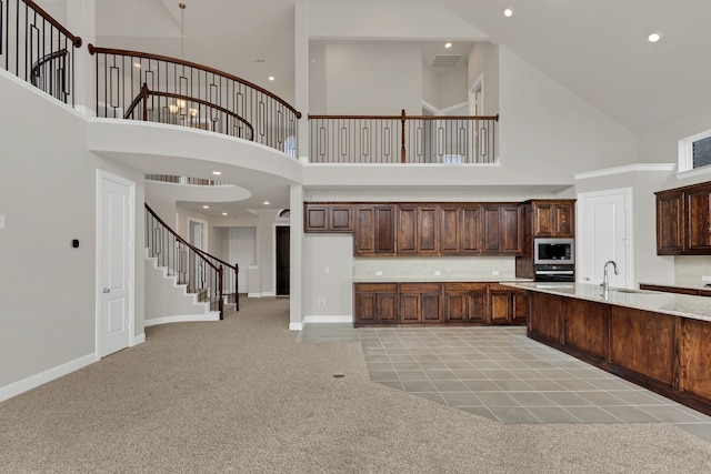 kitchen with dark brown cabinets, light colored carpet, a towering ceiling, and built in microwave