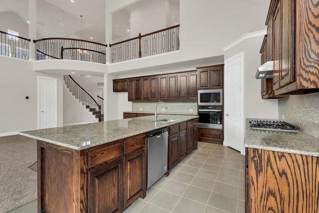 kitchen with a towering ceiling, tasteful backsplash, light stone counters, stainless steel appliances, and exhaust hood