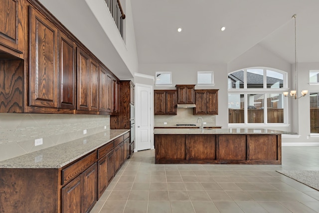 kitchen with light stone countertops, tasteful backsplash, high vaulted ceiling, a chandelier, and dark brown cabinets