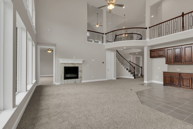 unfurnished living room featuring a high end fireplace, ceiling fan, tile patterned floors, and a high ceiling