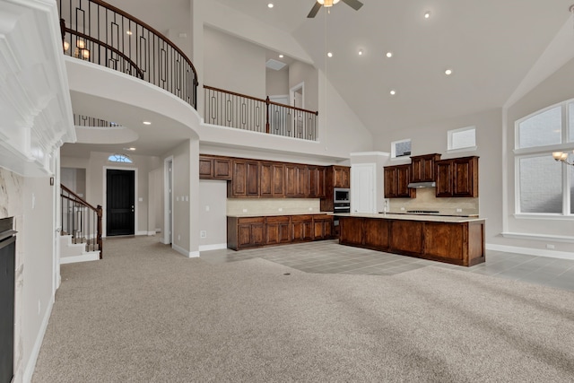 unfurnished living room featuring light carpet, a towering ceiling, ceiling fan with notable chandelier, and sink