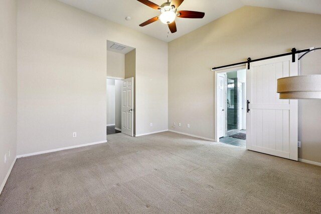 carpeted empty room with ceiling fan, a barn door, and vaulted ceiling