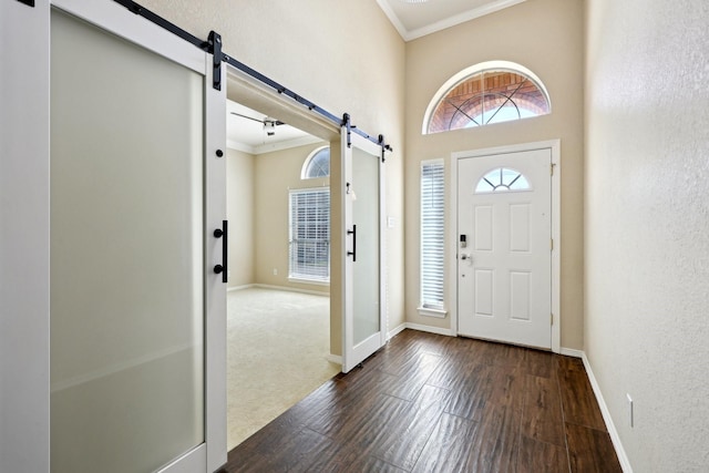 entrance foyer featuring dark wood-type flooring, ornamental molding, and a barn door