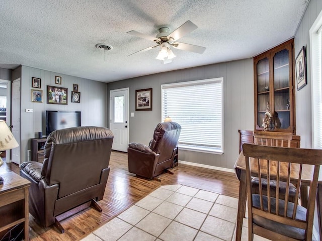 living room with ceiling fan, light hardwood / wood-style flooring, and a textured ceiling