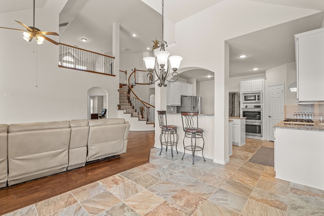 kitchen featuring backsplash, high vaulted ceiling, ceiling fan with notable chandelier, white cabinetry, and stainless steel appliances