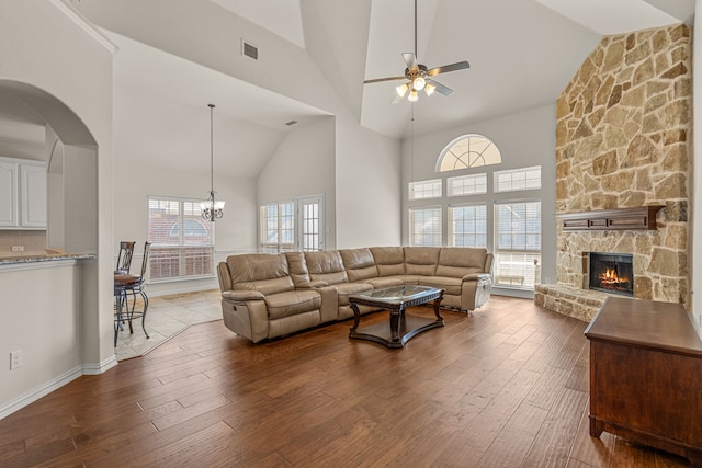 living room featuring a stone fireplace, dark hardwood / wood-style flooring, high vaulted ceiling, and ceiling fan with notable chandelier