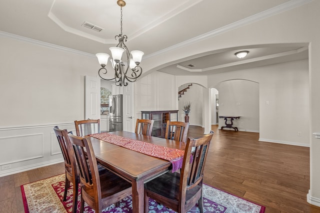 dining area with an inviting chandelier, a raised ceiling, dark wood-type flooring, and crown molding