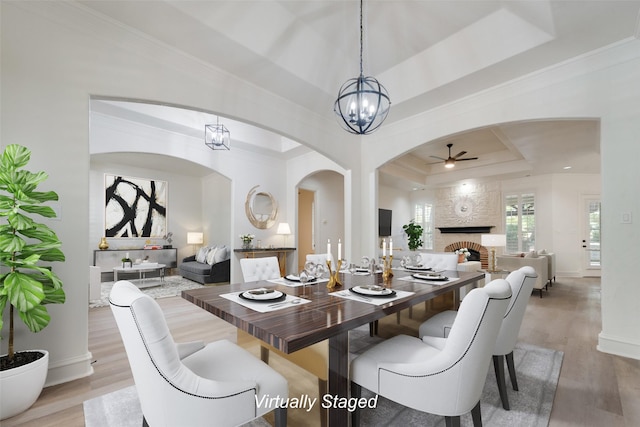 dining area with a raised ceiling, light hardwood / wood-style flooring, and ceiling fan with notable chandelier