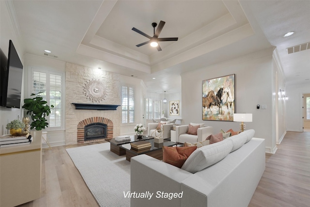 living room with ceiling fan, a raised ceiling, light hardwood / wood-style flooring, a fireplace, and ornamental molding