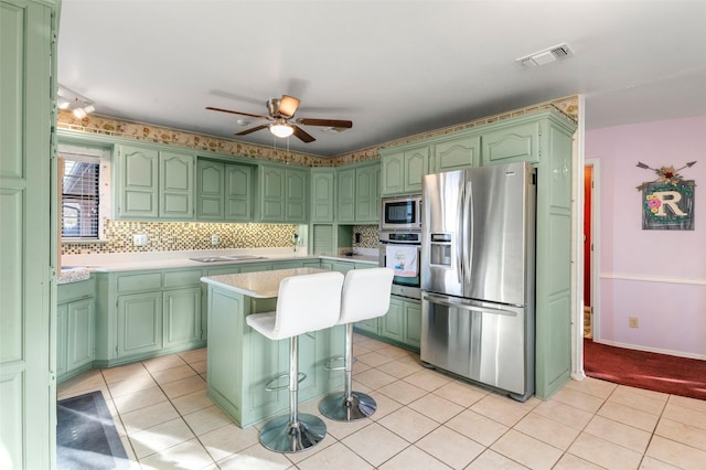 kitchen featuring a center island, backsplash, ceiling fan, light tile patterned flooring, and stainless steel appliances