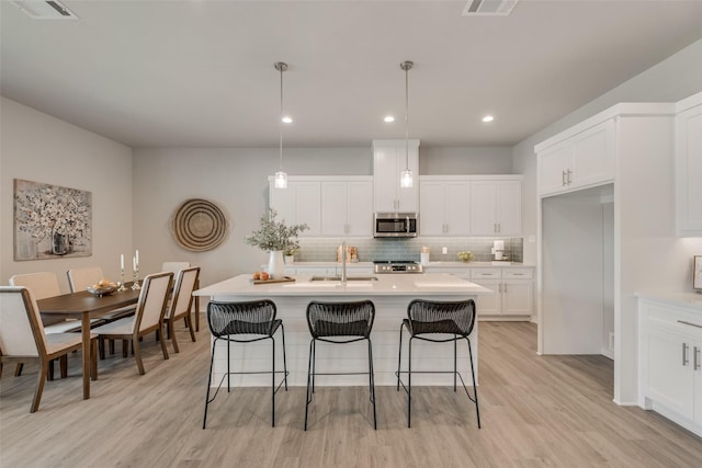 kitchen with decorative light fixtures, sink, stainless steel appliances, and an island with sink