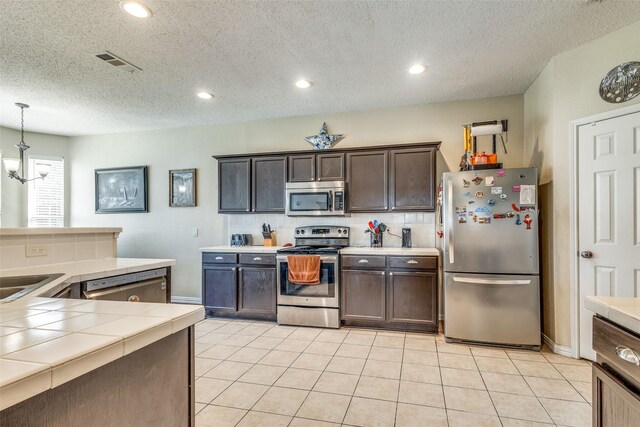 kitchen with decorative backsplash, appliances with stainless steel finishes, dark brown cabinets, a textured ceiling, and pendant lighting