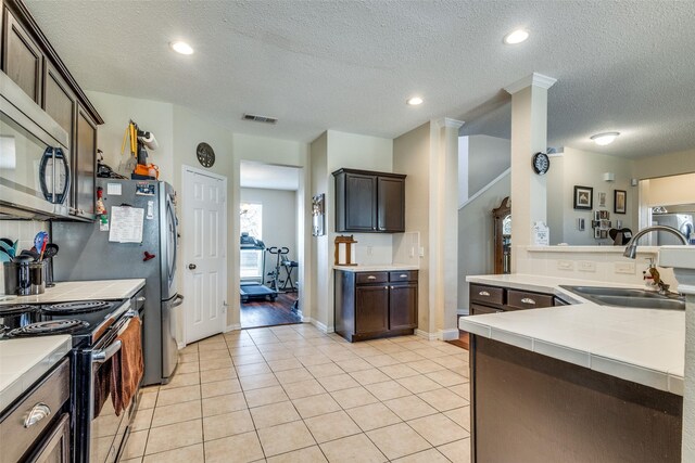 kitchen featuring dark brown cabinets, sink, light tile patterned floors, and a textured ceiling