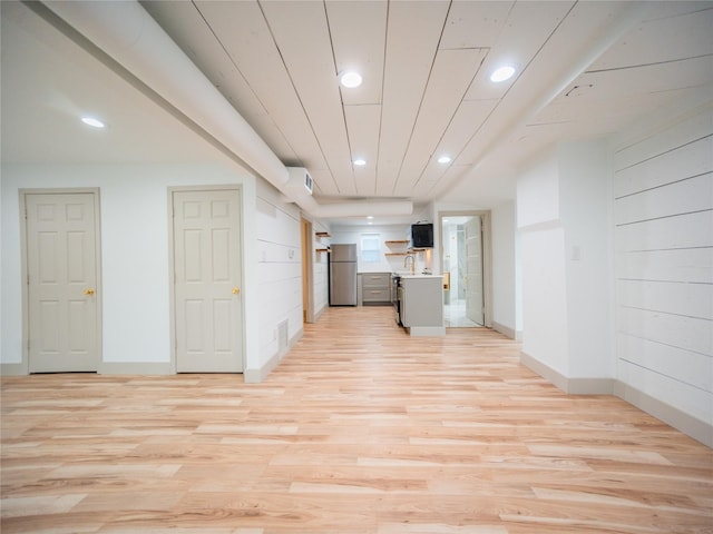 interior space with stainless steel refrigerator, sink, wood walls, light hardwood / wood-style floors, and a kitchen island