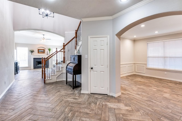 foyer entrance featuring ceiling fan with notable chandelier, ornamental molding, and parquet flooring