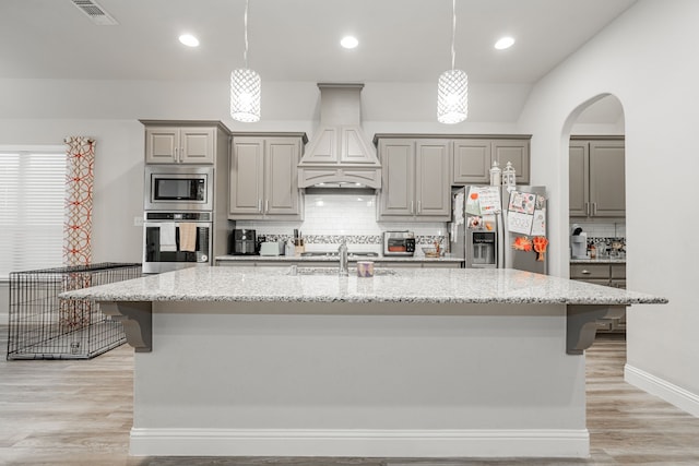 kitchen featuring premium range hood, light stone counters, stainless steel appliances, sink, and an island with sink