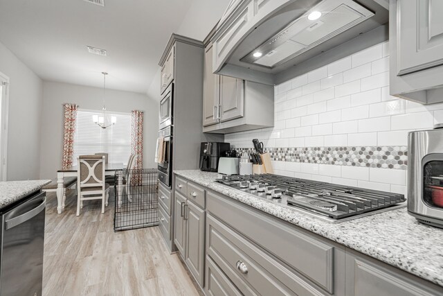 kitchen featuring light wood-type flooring, tasteful backsplash, stainless steel appliances, a chandelier, and range hood