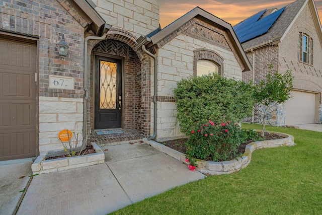 exterior entry at dusk featuring a yard and a garage