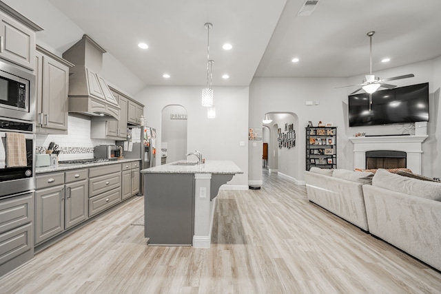 kitchen with backsplash, gray cabinets, an island with sink, and appliances with stainless steel finishes