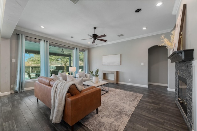 living room with ceiling fan, dark hardwood / wood-style flooring, a stone fireplace, and crown molding