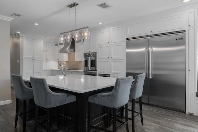 kitchen with a breakfast bar area, appliances with stainless steel finishes, pendant lighting, white cabinets, and wall chimney range hood