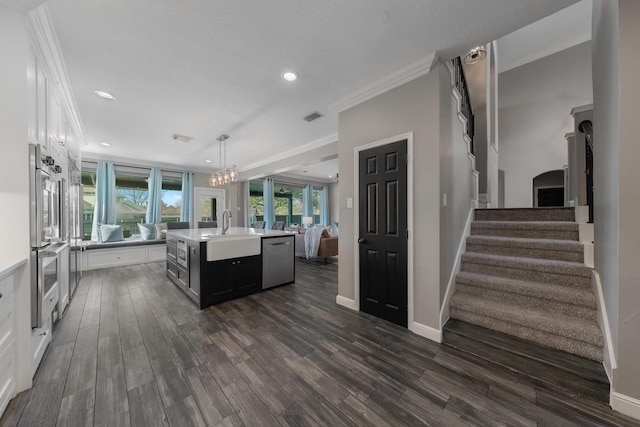 kitchen with hanging light fixtures, stainless steel appliances, a center island with sink, white cabinetry, and sink